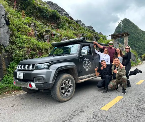 Happy customers standing next to an open top jeep, on the road in Ha Giang