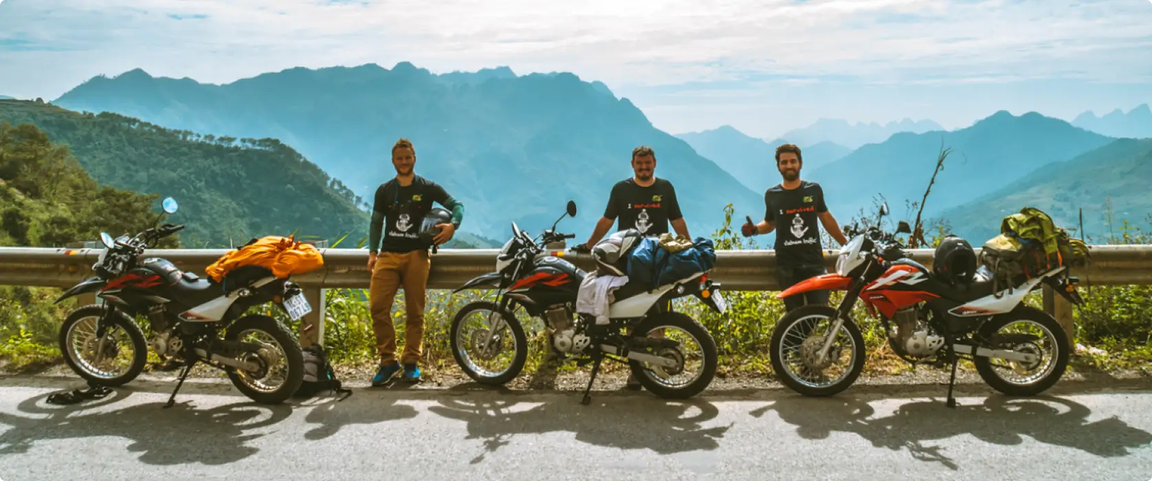 Three men standing next to Honda XR 150 motorcylces with a view of mountains behind them