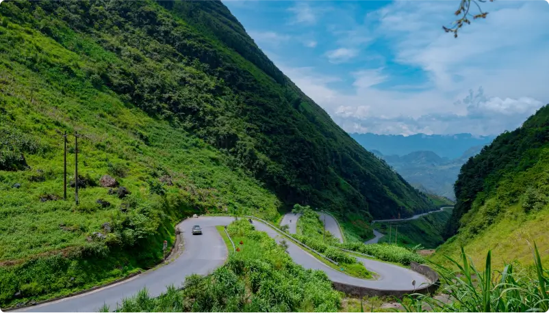 a view of the Ma Pi Leng Pass in Ha Giang with a winding road in the foreground and green mountains in the back