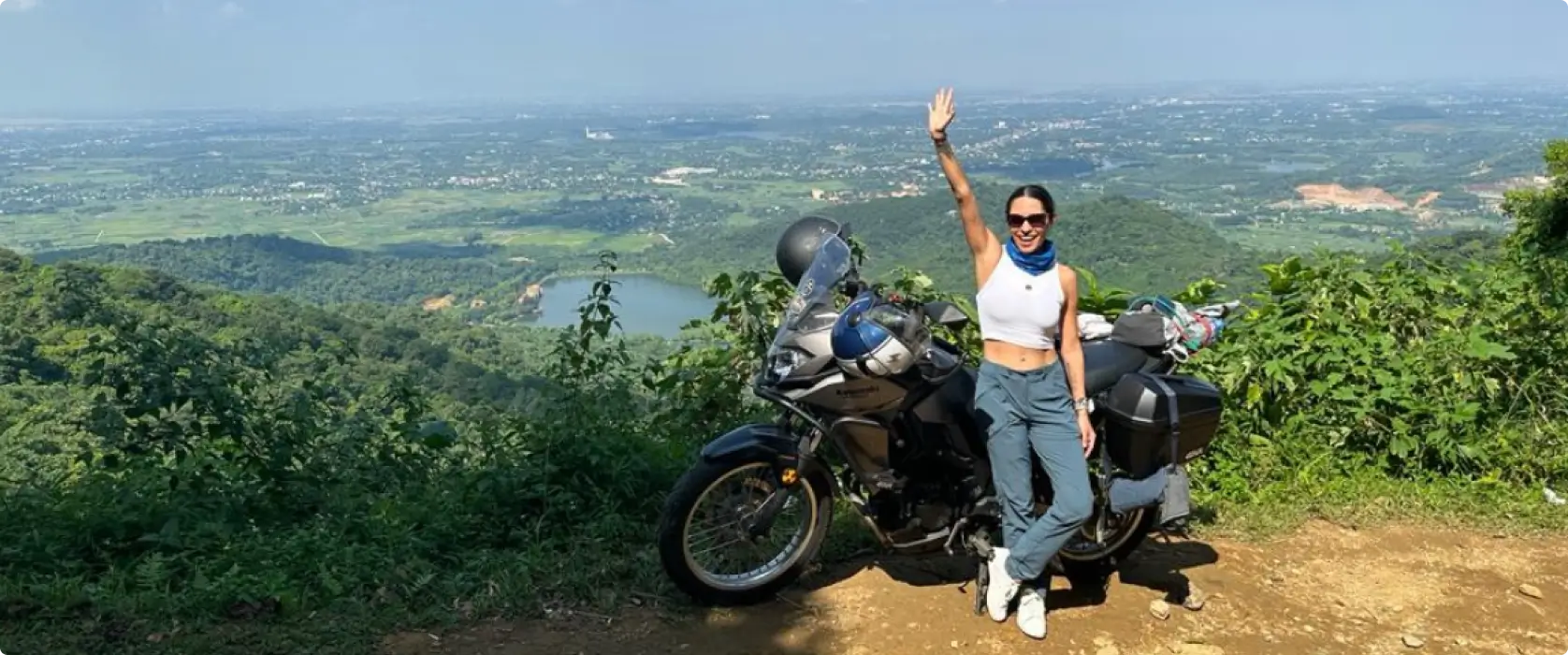 A woman smiling next to a parked motorcycle in Ba Vi National Park, Vietnam