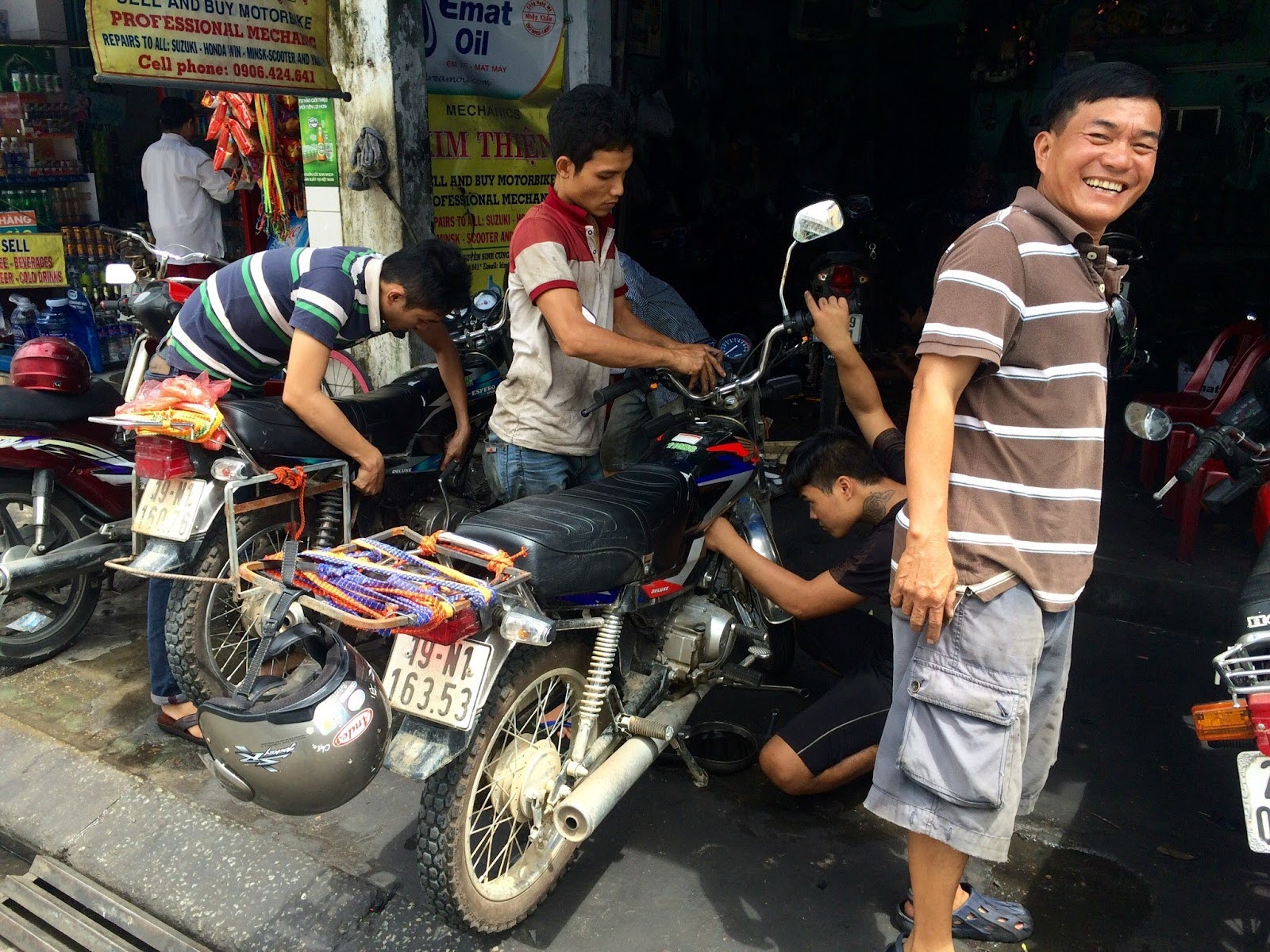 Mechanics inspecting and repairing a motorbike at a roadside workshop in Vietnam.